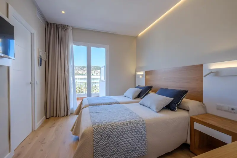Chambre lumineuse avec un grand lit et un accès à un balcon.
