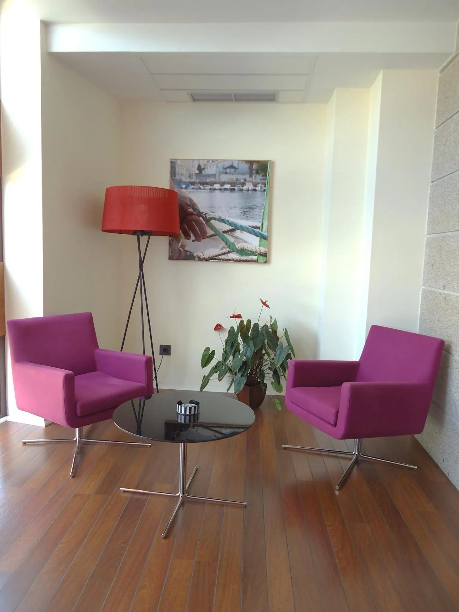 Deux fauteuils violets et une table basse en verre sont disposés dans un espace lumineux avec un parquet en bois.