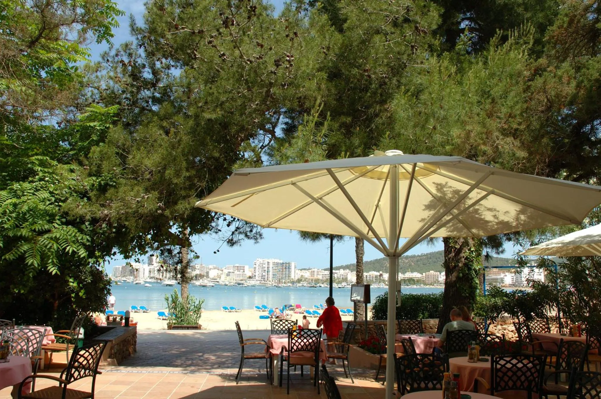 Terrasse ombragée avec tables et chaises donnant sur une plage.