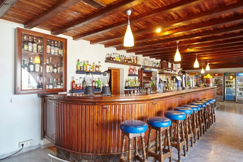 Un long comptoir en bois est aligné de tabourets bleus et de bouteilles.