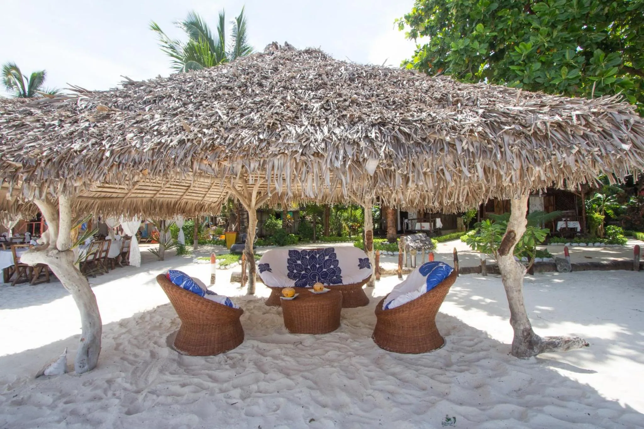 Espace de détente ombragé avec mobilier en rotin sur sable blanc.