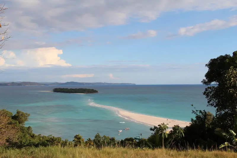 Vue aérienne d'une plage de sable blanc et d'eaux turquoise bordée d'une végétation luxuriante.