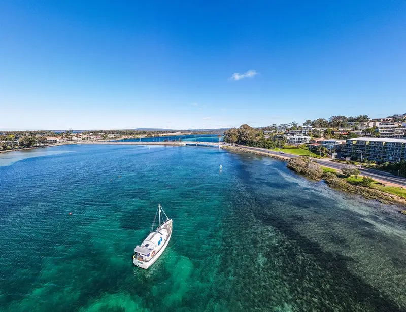 Vue aérienne d'une côte avec un bateau à voile et une étendue d'eau turquoise.