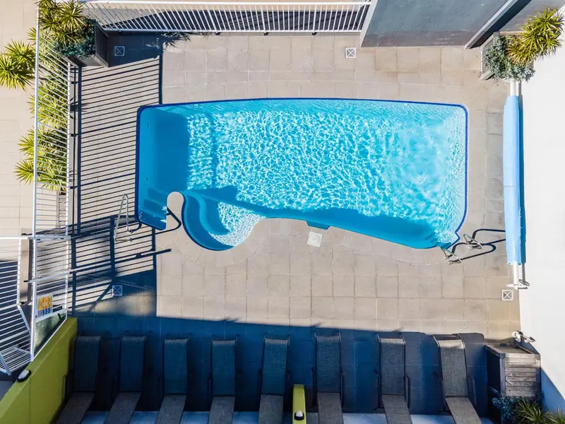 Vue aérienne d'une piscine rectangulaire avec un toboggan et des transats.