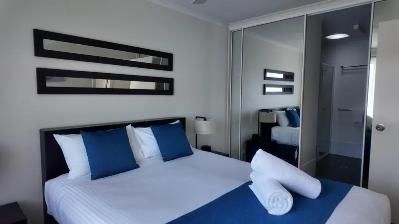 Une chambre avec un grand lit recouvert d'une couette blanche et de coussins bleus.