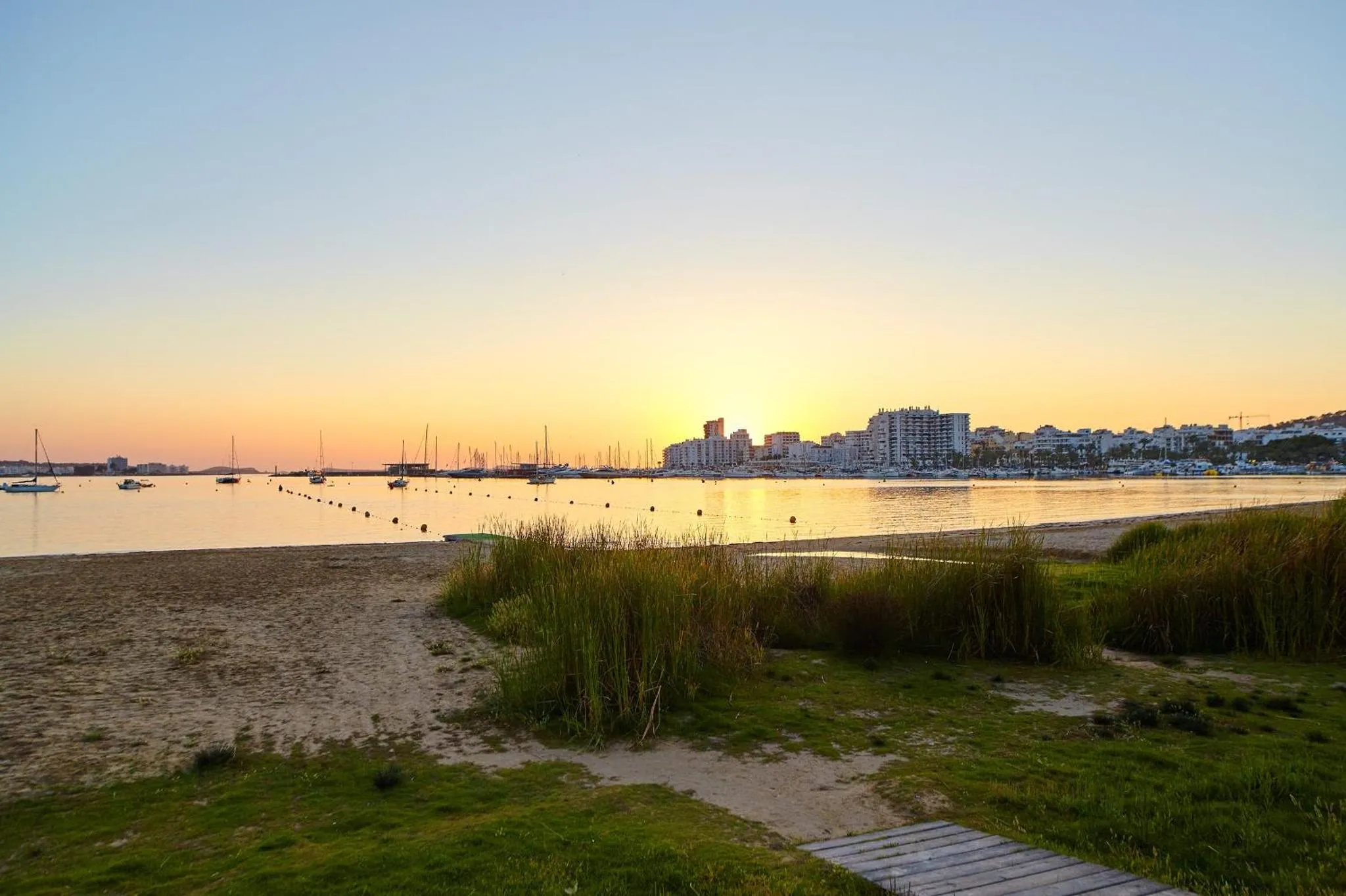 Plage de sable fin au coucher du soleil, avec une vue sur la mer et la ville en arrière-plan.