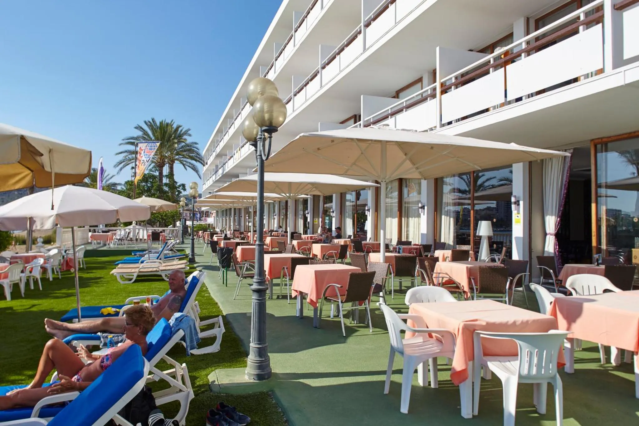 Terrasse ombragée avec tables et chaises, donnant sur une pelouse et des transats.