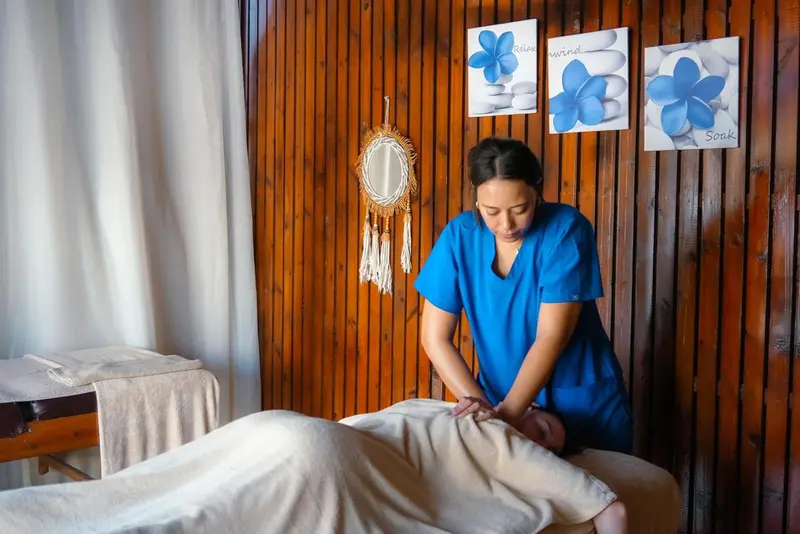 Une femme reçoit un massage sur une table recouverte d'une serviette dans une pièce aux murs lambrissés.