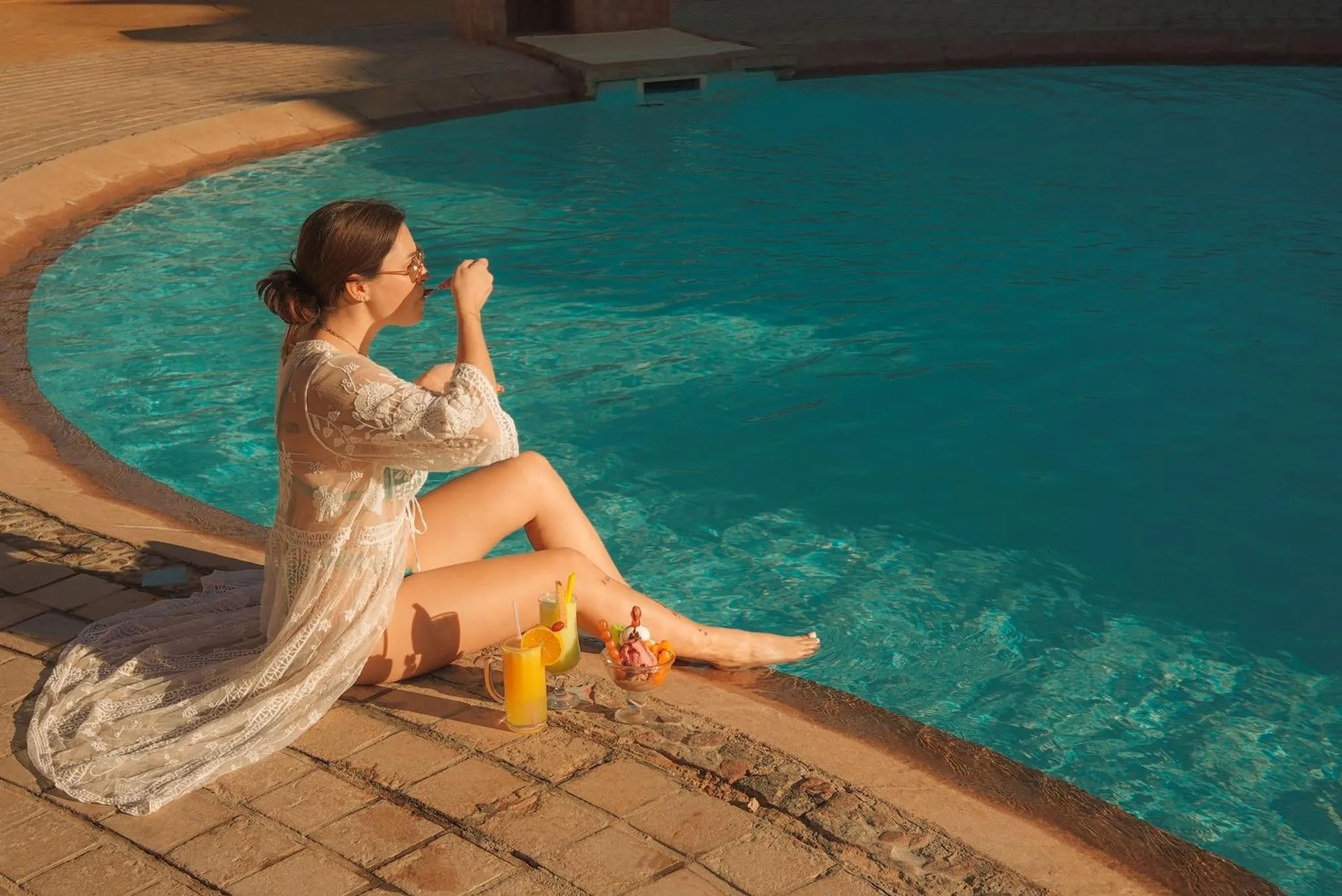 Une femme se détend au bord d'une piscine ensoleillée avec des boissons.