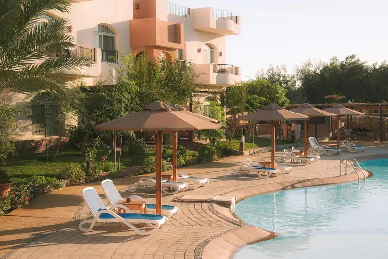 Transats et parasols bordent une piscine turquoise dans un jardin soigné.