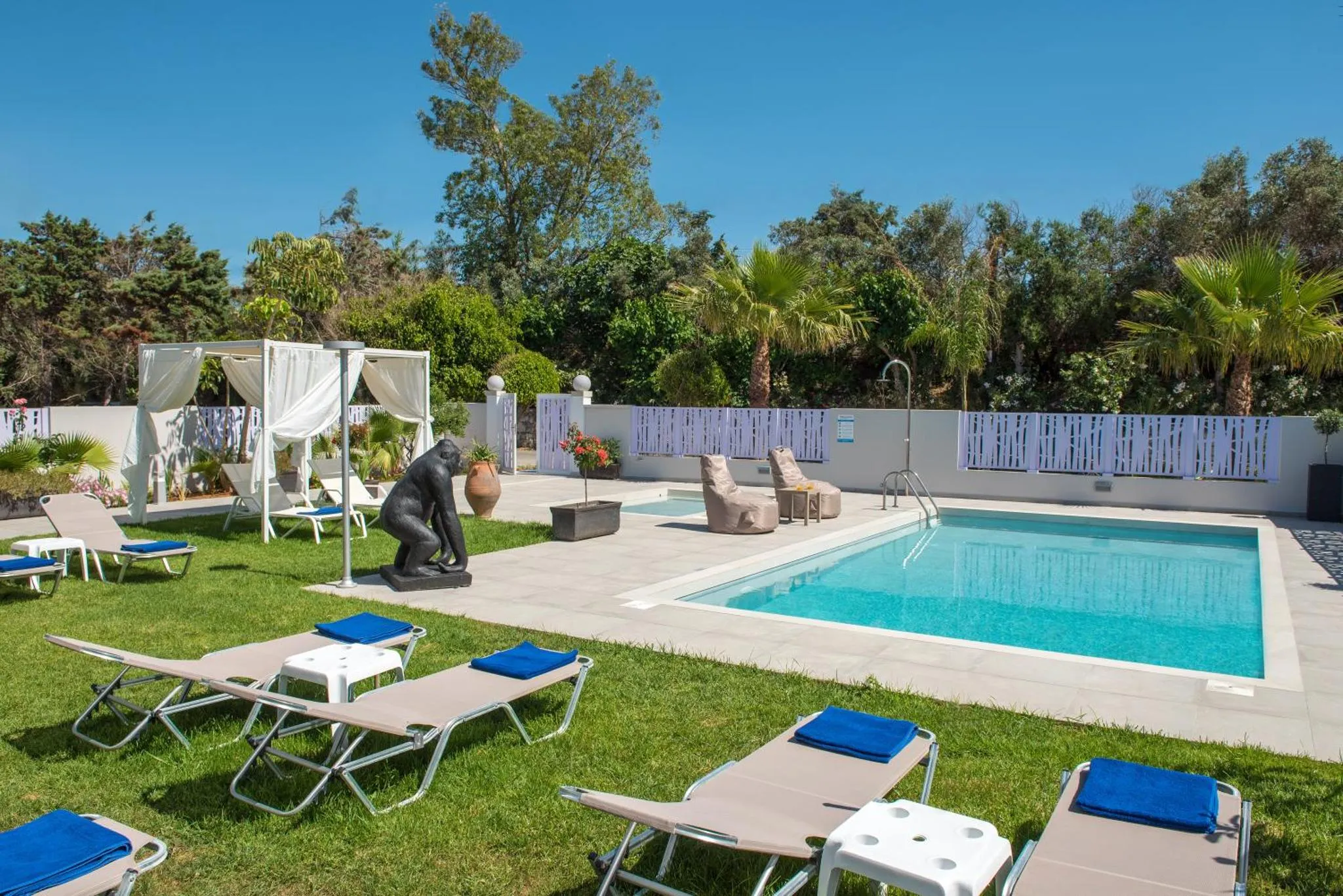 Transats bleus disposés autour d'une piscine rectangulaire dans un jardin verdoyant.