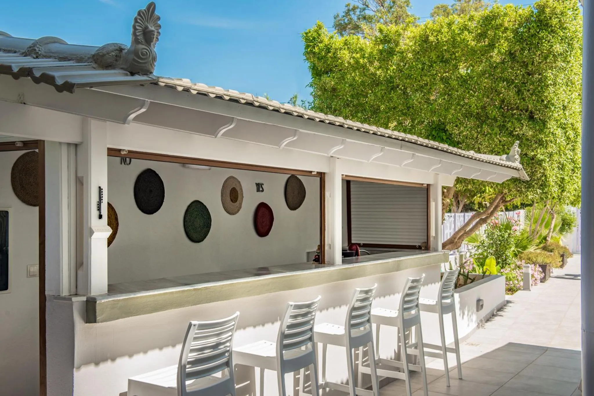 Un bar extérieur avec des tabourets blancs et une décoration murale.