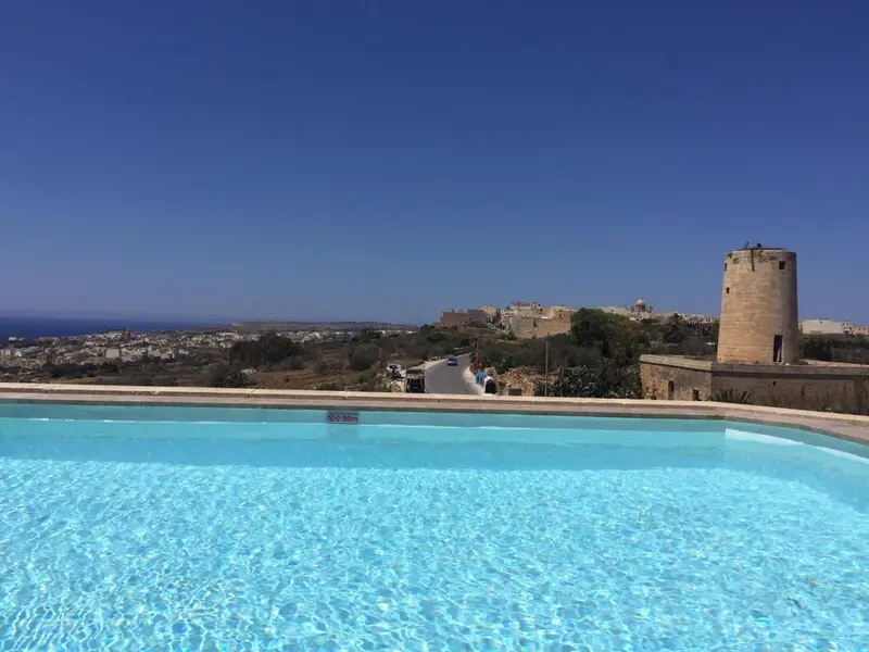 Piscine bleue au premier plan avec une vue sur un village et une tour.