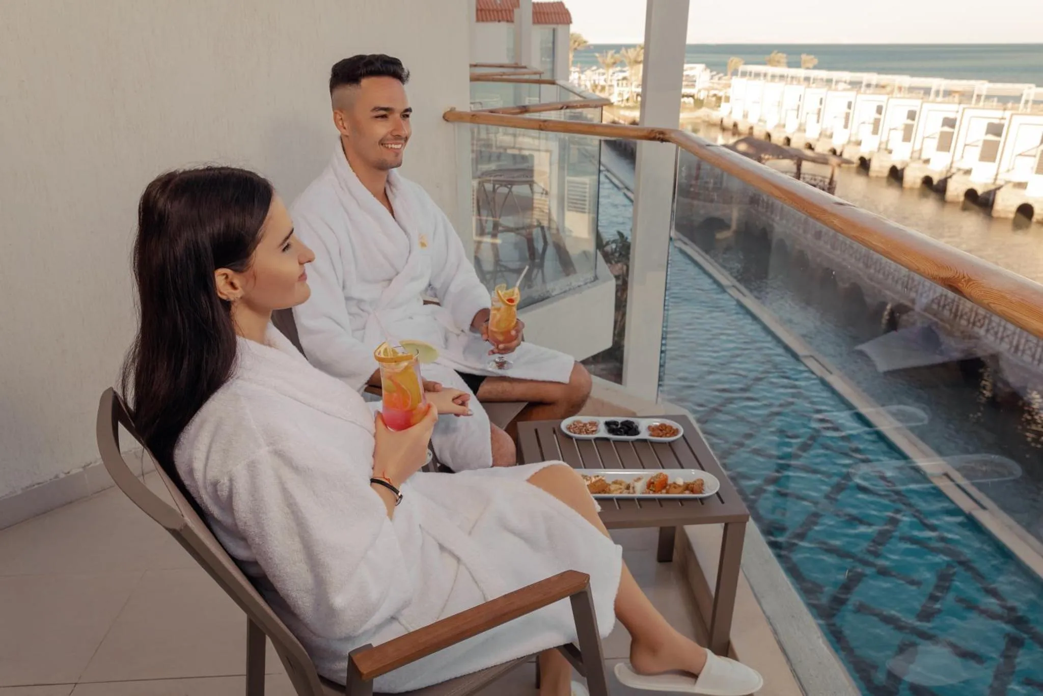 Un couple profite de boissons et de viennoiseries sur un balcon avec vue sur la mer.