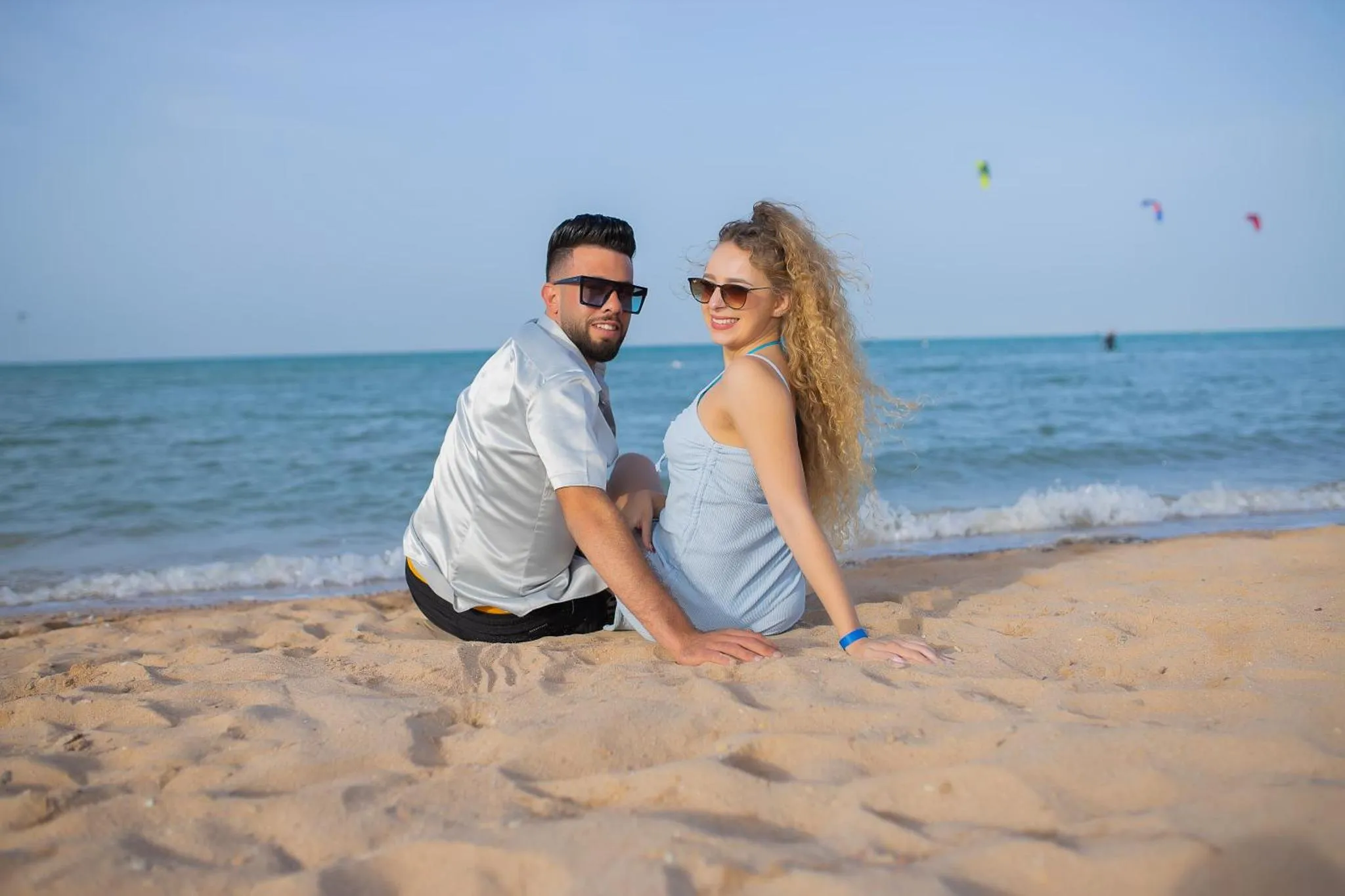 Un couple souriant est assis sur une plage de sable fin, face à la mer.