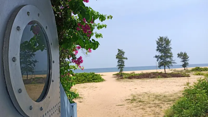 Une vue sur une plage de sable fin et la mer, encadrée par une fenêtre ronde ornée de fleurs.