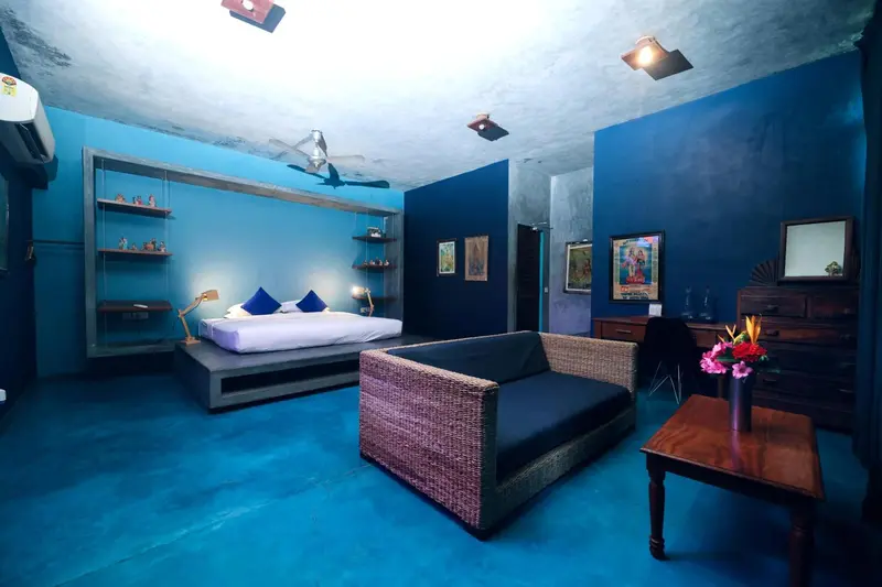 Une chambre spacieuse aux murs bleus est aménagée avec un lit, un canapé et des étagères.