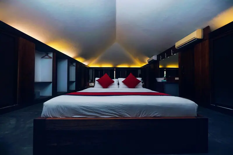 Une chambre lumineuse avec un grand lit recouvert d'une couette blanche et de coussins rouges.