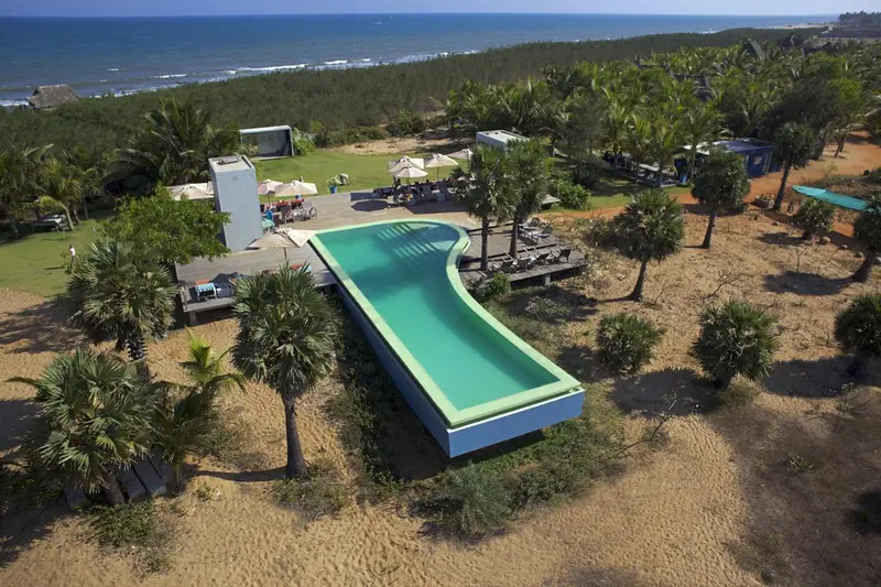 Vue aérienne d'une piscine sinueuse bordée de palmiers et de transats.