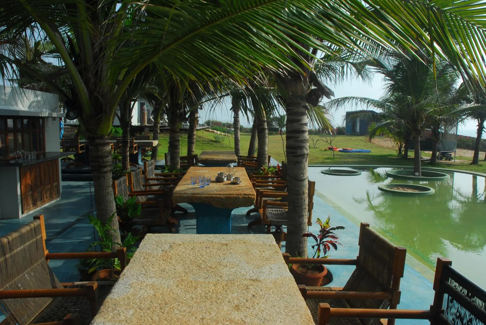 Tables et chaises disposées sur une terrasse ombragée près d'une piscine.