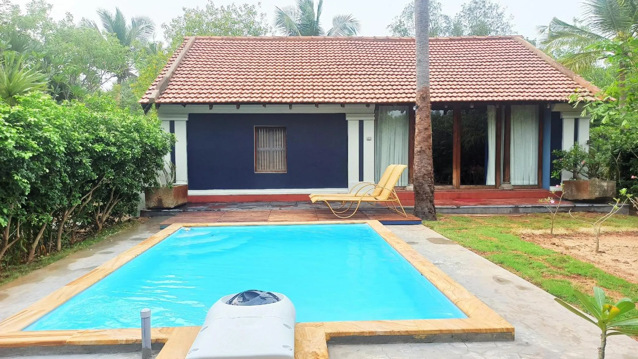 Bâtiment bleu avec piscine et transats dans un jardin tropical.