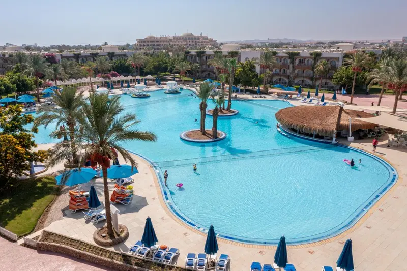 Vue aérienne d'une grande piscine d'hôtel entourée de transats et de végétation.