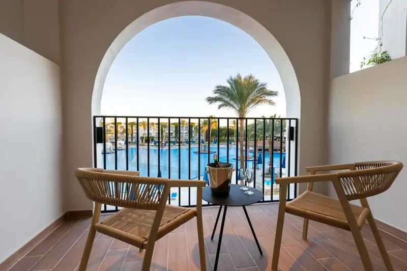 Une terrasse avec deux fauteuils en osier et une table basse donne sur une vue tropicale.