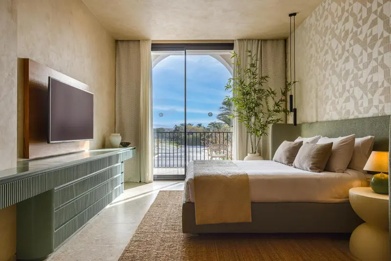 Chambre lumineuse avec un grand lit et vue sur un jardin.