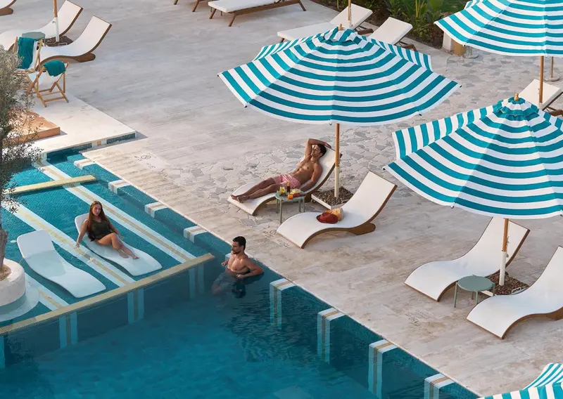 Des transats rayés turquoise et blancs ombragent une piscine ensoleillée.