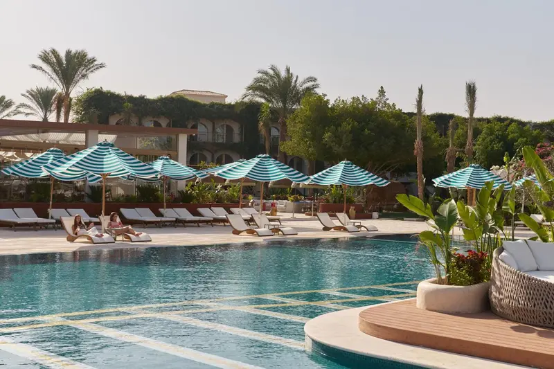 Transats bleus et blancs disposés autour d'une piscine turquoise bordée de végétation luxuriante.