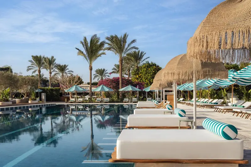 Transats blancs alignés au bord d'une piscine turquoise sous des parasols rayés.