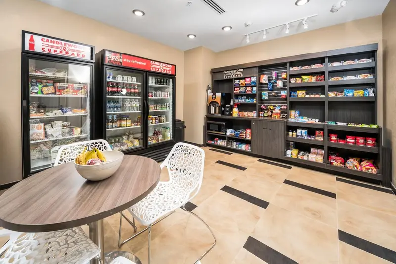 Une table ronde est entourée de chaises blanches devant des étagères remplies de produits.