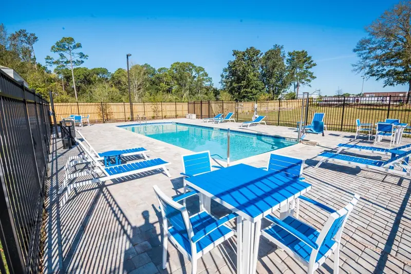Une piscine rectangulaire bordée de chaises longues et de tables bleues sous un ciel bleu dégagé.