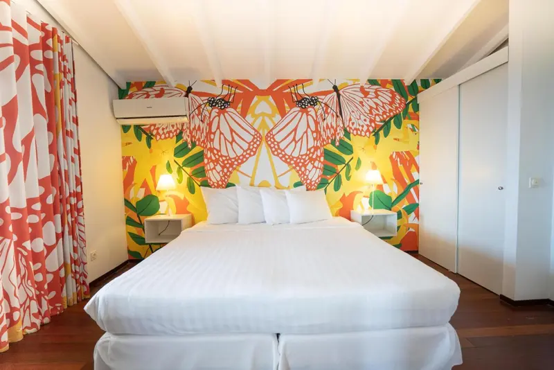 Une chambre lumineuse avec un grand lit blanc et un mur décoré de motifs de papillons.