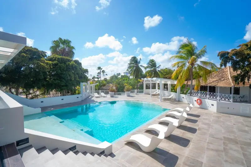 Une piscine turquoise bordée de chaises longues et de végétation tropicale.