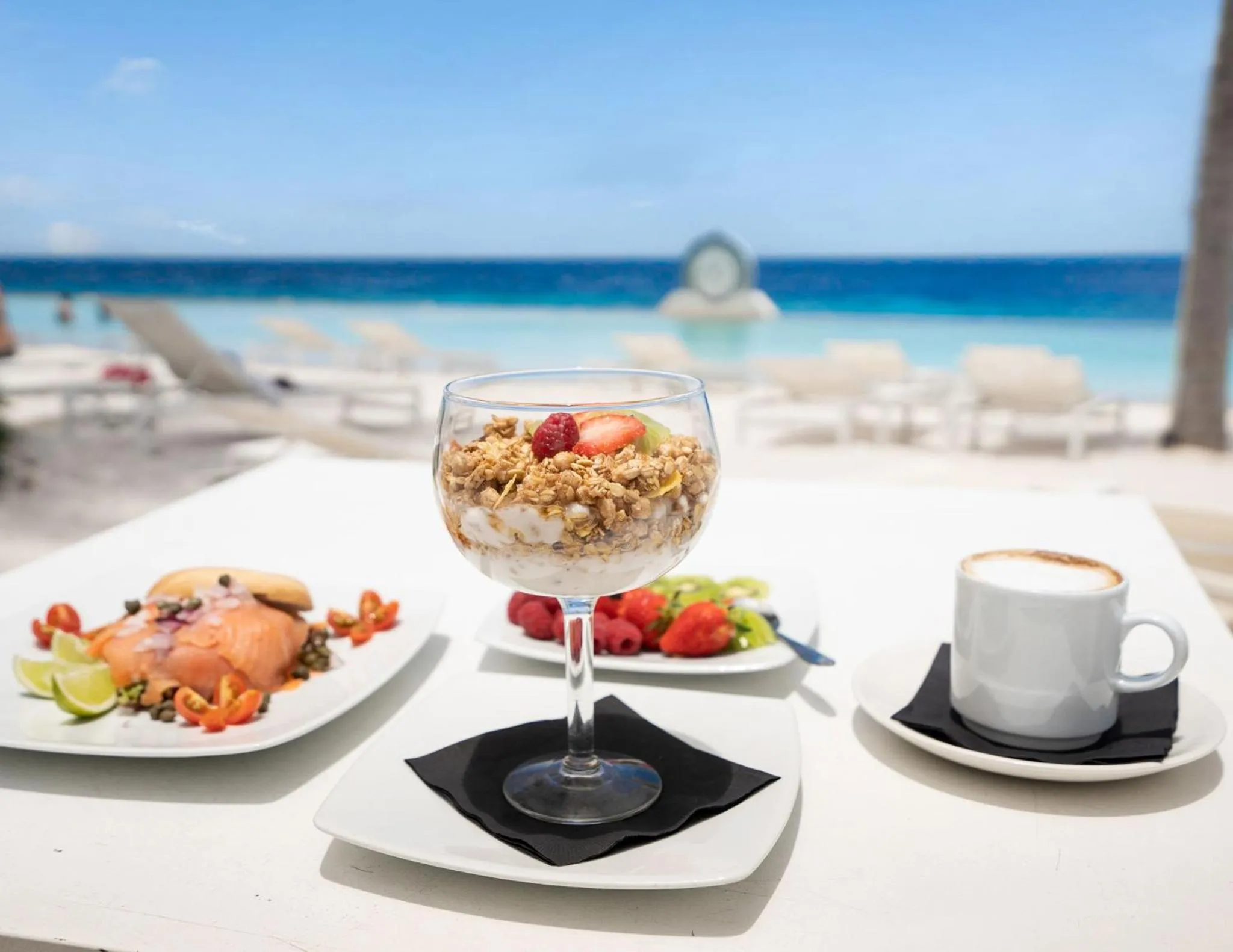 Un petit-déjeuner copieux est servi sur une table blanche en bord de mer.