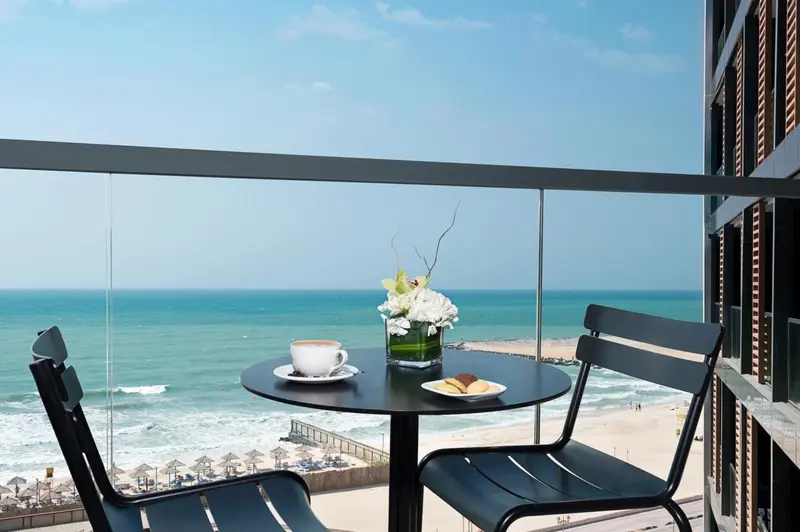 Une table avec une tasse de café et des pâtisseries sur un balcon avec vue sur la mer.