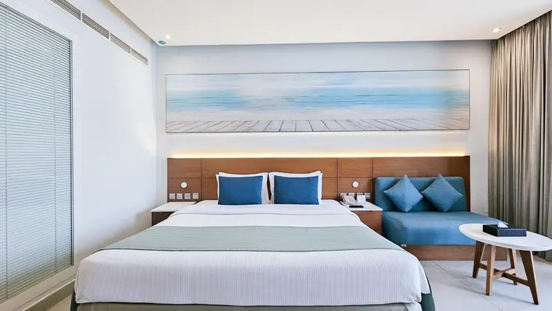 Chambre lumineuse avec un grand lit et un coin salon bleu.
