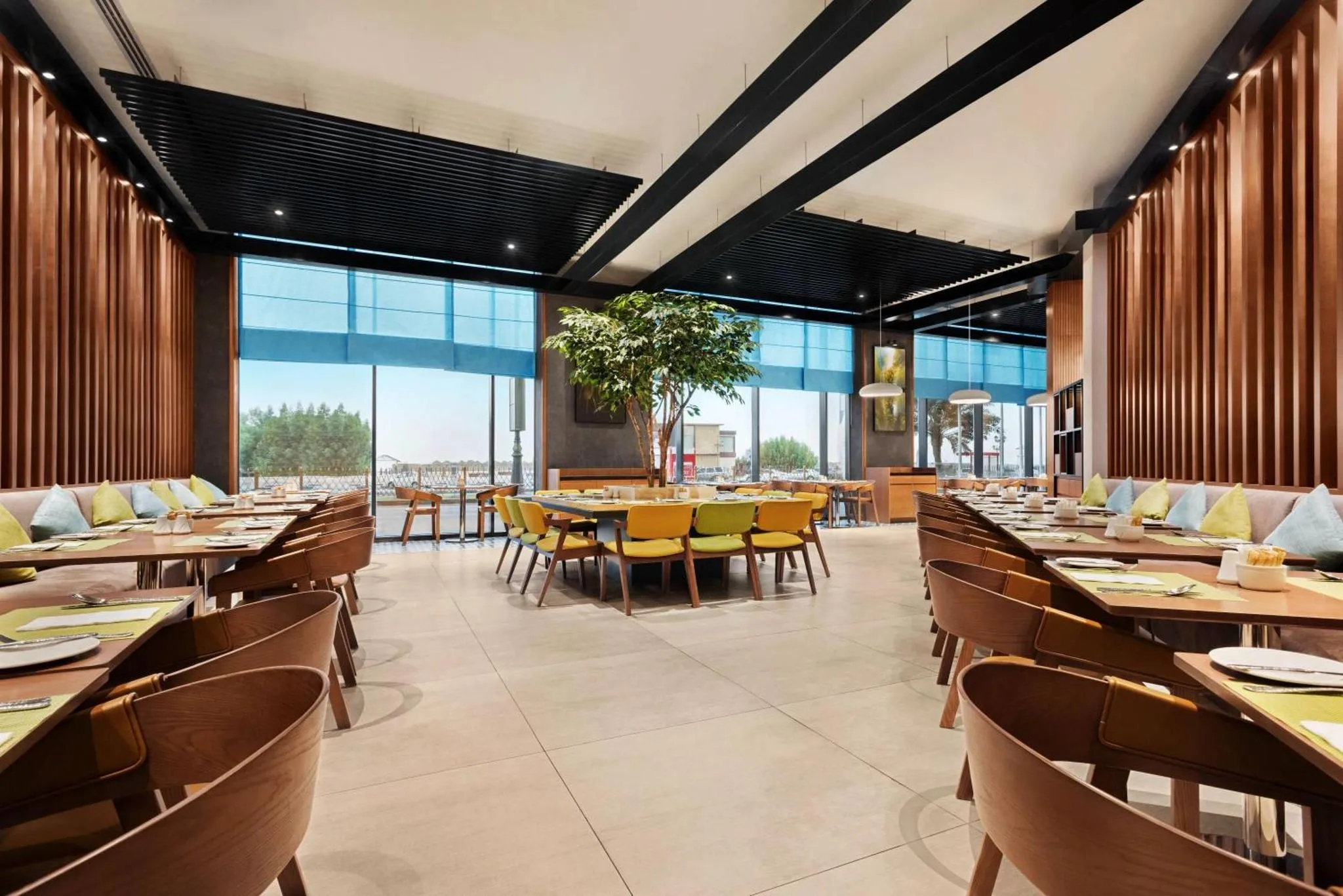 Une salle lumineuse avec des tables dressées et des banquettes en bois.