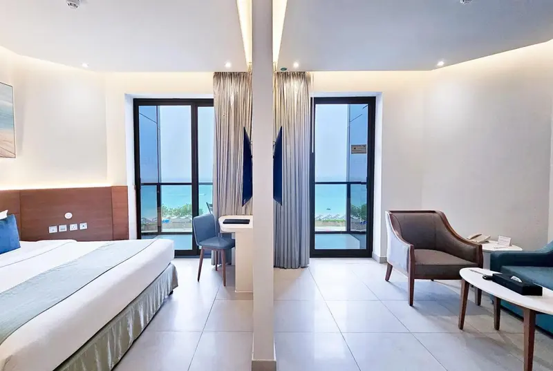 Chambre lumineuse avec un lit et un coin salon donnant sur la mer.