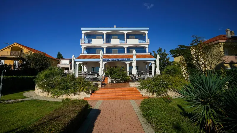 Façade d'un bâtiment blanc à deux étages avec des balcons et une terrasse ombragée.