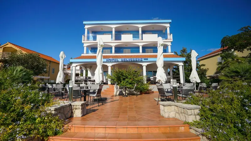 Façade d'un bâtiment blanc et bleu avec une terrasse ombragée et des tables.