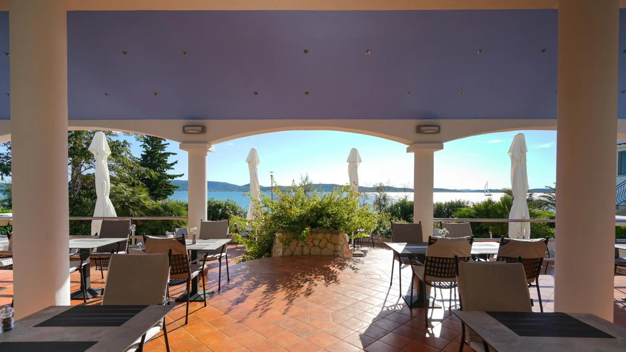 Terrasse ombragée avec tables et chaises donnant sur la mer.