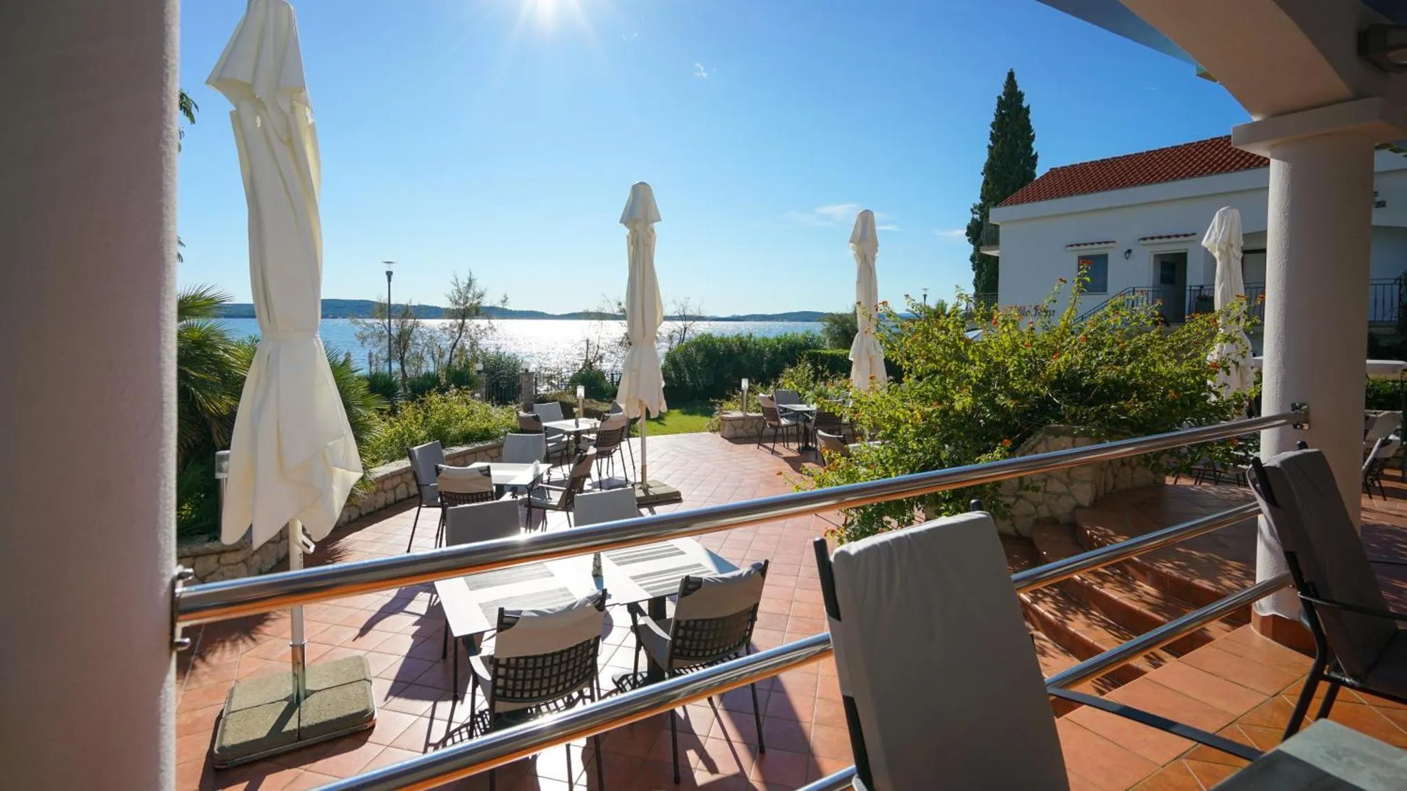 Terrasse ombragée avec tables et chaises donnant sur la mer.