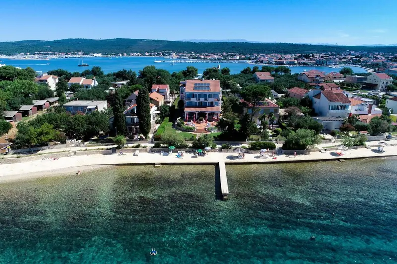 Vue aérienne d'une plage bordée de bâtiments et de végétation luxuriante.