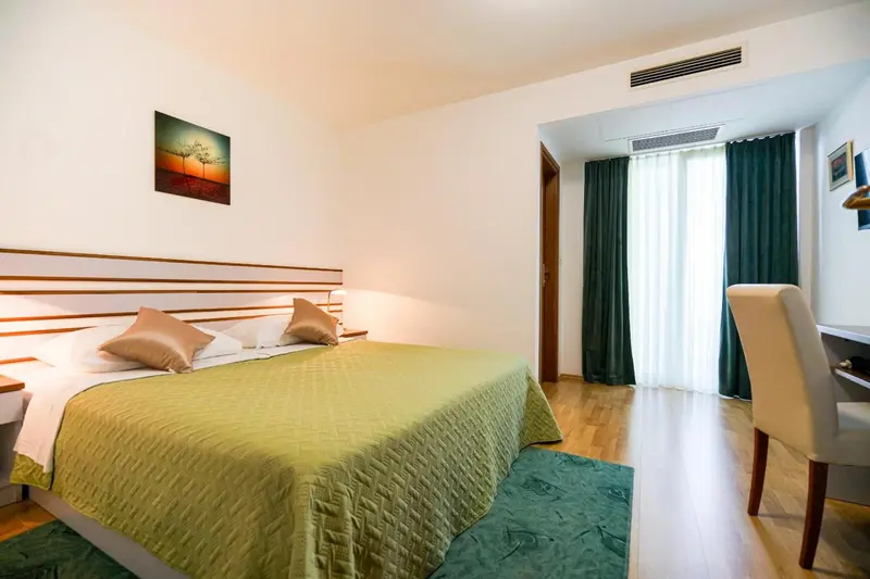Une chambre lumineuse avec un grand lit recouvert d'une couette verte et de coussins.