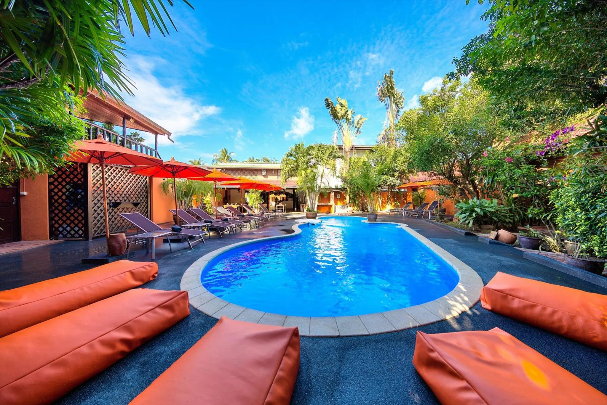 Transats orange disposés autour d'une piscine bleue dans un jardin tropical.