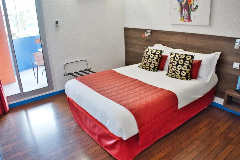 Une chambre lumineuse avec un lit recouvert d'une courtepointe rouge et blanche.