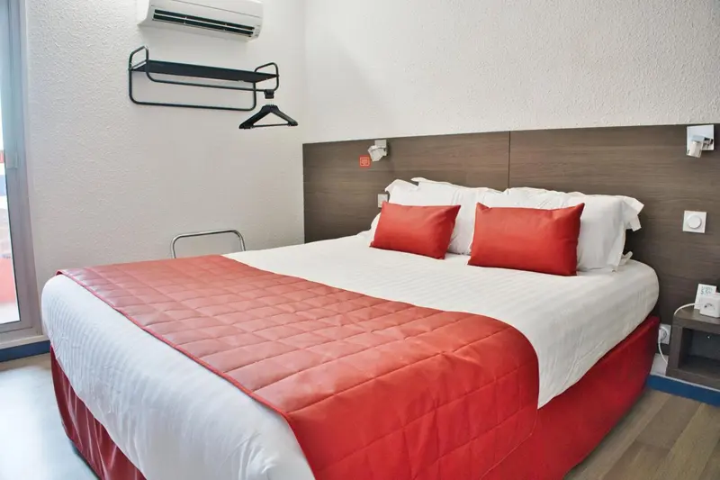 Une chambre lumineuse avec un lit double recouvert d'une courtepointe rouge et de coussins assortis.