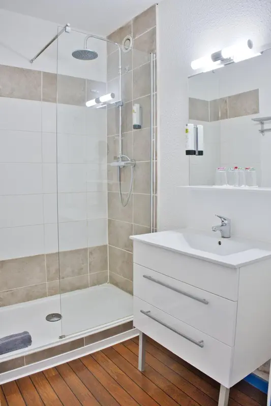 Une douche à l'italienne avec un lavabo blanc et un carrelage beige.